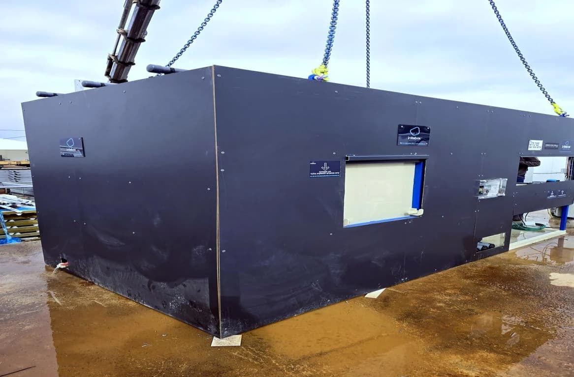 יחידת INFRABOX שחורה תלויה בשרשראות המנוף בעת הורדתה אל המשטח המוכן שלה.