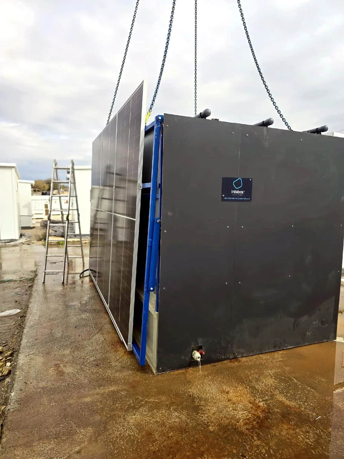 יחידת INFRABOX שחורה תלויה בשרשראות מנוף ומורדת אל המשטח המוכן שלה
