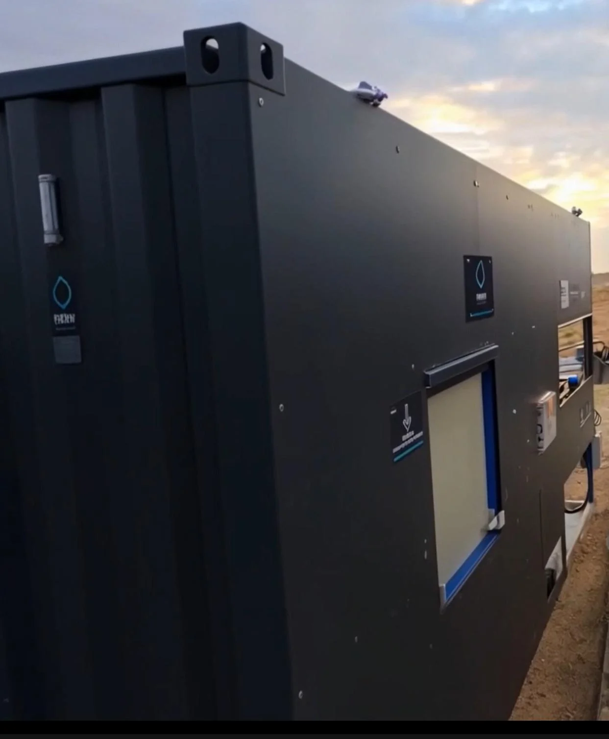A black INFRABOX treatment unit standing on its pad at sunset, its corner casting and door placards against a clouded sky.